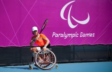 Paralympics-Sportlerin Marjolein Buis mit Tennisschläger im Rollstuhl vor Paralympics-Plakat in London 2012