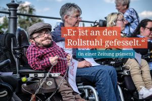 Ein Rollstuhlfahrer schaut in die Kamera und hat eine Kette in der Hand. Daneben steht der Text: "Er ist an den Rollstuhl gefesselt."