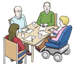 An einem Tisch sitzen zwei Männer, eine Frau und ein Rolstuhlfahrer. Sie sprechen miteinander.
