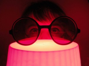 Person schaut durch eine rote Brille, die von einer Lampe angeleuchtet wird.