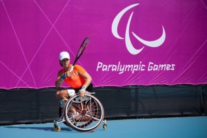 Paralympics-Sportlerin Marjolein Buis mit Tennisschläger im Rollstuhl vor Paralympics-Plakat in London 2012