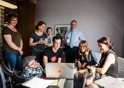 Eine Gruppe von Menschen steht und sitzt vor einem Laptop und schaut darauf.