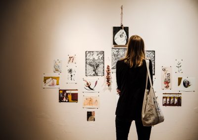 Eine Wand mit Malereien ist zu sehen und eine Frau mit dem Rücken zur Kamera, die sich die Kunstwerke anschaut.