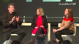 Screenshot aus einem Video. Das Bild zeigt drei Personen (ein Mann (Uwe Hauck) und zwei Frauen) auf einer Bühne der re:publica (Konferenzen zu den Themen der digitalen Gesellschaft) vor Publikum.