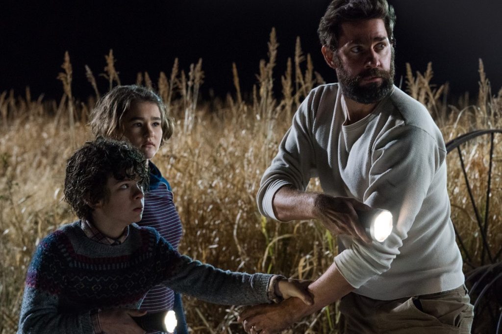 Ein Vater steht verängstigt in einem Kornfeld und hält seinen Sohn in der Hand, in der anderen eine Taschenlampe, seine Tochter steht daneben.