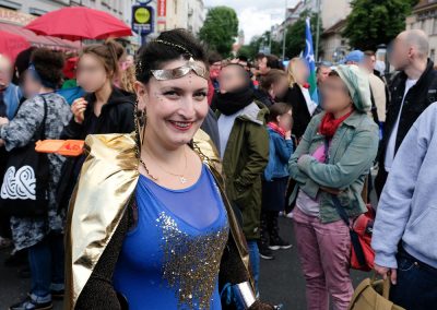 Eine gehbehinderte Demonstrantin ist wie eine Superheldin gekleidet. Im Hintergrund sind weitere Demonstrierende zu sehen.