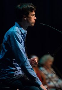 Dirk Sorge hält eine Rede auf der Bühne.Er trägt ein hellblaues Hemd, eine dunkle Hose und hat braune kurze Haare. Auf dem Foto ist er von der Seite zu sehen, wie er in ein Mikrophon spricht.