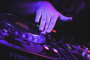 Ein DJ Pult ist blau angeleuchtet. Eine Hand bewegt die Schallplatte.